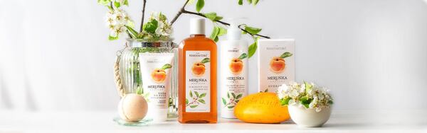 Kozmetické produkty Manufaktura s marhuľou, obklopené kvetmi a vetvičkami stromu, na svetlom pozadí.