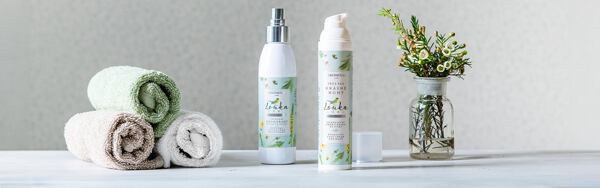 Dezodorant a balzam na nohy Manufaktura Lúka s uterákmi a fľaštičkou s kvetinami na svetlom pozadí.