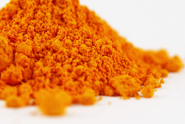 Sypká hmota sýto oranžového prírodného minerálneho pigmentu na bielom povrchu.
