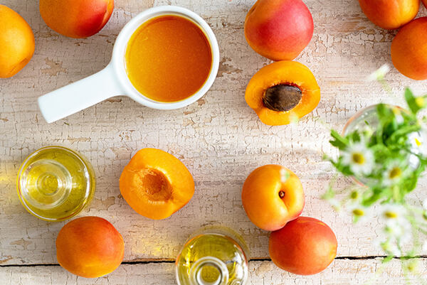 Čerstvé marhule, marhuľový olej a miska s dužinou na drevenom stole.