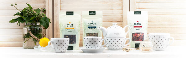 Bylinné a ovocné čaje Manufaktura s bodkovaným porcelánom, kanvičkou a citrónom na svetlom pozadí.