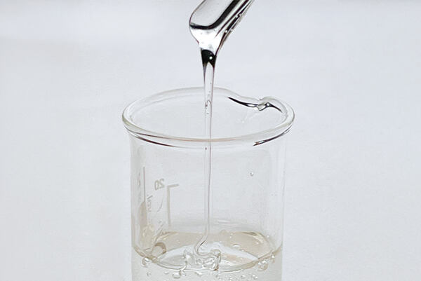 Priehľadný gél stekajúci z kovovej špachtle do laboratórnej odmerky.