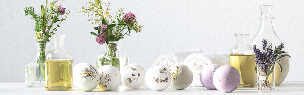 Šumivé gule do kúpeľa Manufaktura v rôznych farbách s bylinkami, olejmi a uterákmi na svetlom pozadí.