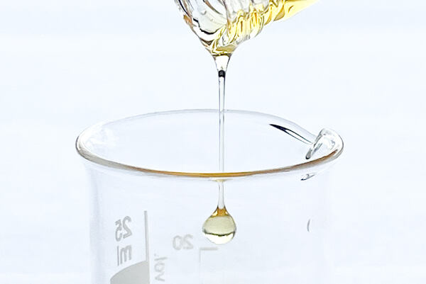 Zlatistá kvapka vitamínu E stekajúca do laboratórneho pohára.