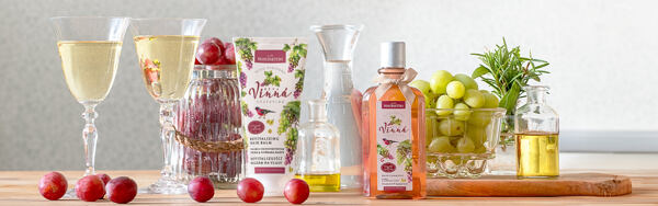 Vínny šampón a balzam Manufaktura obklopený pohármi vína, hroznom a prírodnými ingredienciami na drevenej doske.