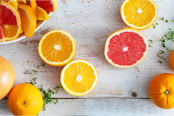 Čerstvo rozkrojené pomaranče a grep na svetlom drevenom podklade.