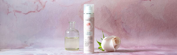 Liftingová maska s ružovým motívom, doplnená ružou a sklenenou fľaštičkou na jemne ružovom pozadí.