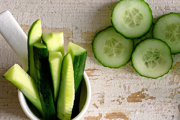 Nakrájaná čerstvá uhorka na plátky a tyčinky v bielej miske na rustikálnom stole.