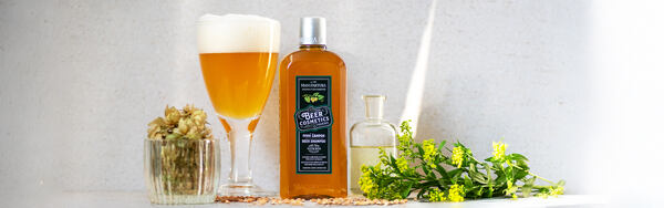 Pivný šampón Manufaktura s pohárom piva, chmeľom, olejom a žltými bylinkami na svetlom pozadí.