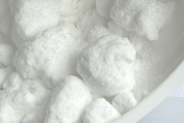 Biele kryštalické hrudky niacínamidu v laboratórnej miske.