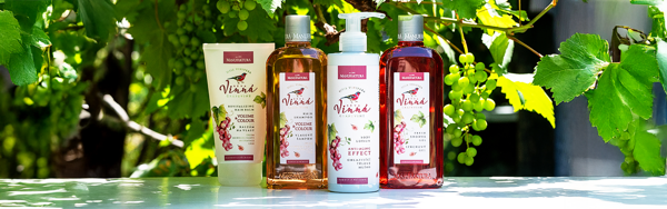 Kozmetické produkty Manufaktura z vínnej kolekcie s hroznom, olejom a bylinkami na drevenom podklade.