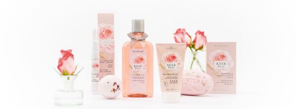 Kozmetické produkty z kolekcie Ruža a Žriedlová soľ značky Manufaktura, obklopené kvetmi ruží a dekoráciami v ružových tónoch.