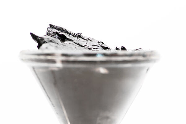 Minerálne bahno z Mŕtveho mora v sklenenej miske na bielom pozadí.