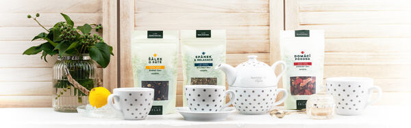 Bodkované hrnčeky, kanvička a lyžička Manufaktura s balenými čajmi a citrónom na svetlom pozadí.