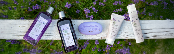 Kozmetická sada s fialovým mydlom, dvomi fľaštičkami a dvomi tubami na drevenej lavičke v záhrade.