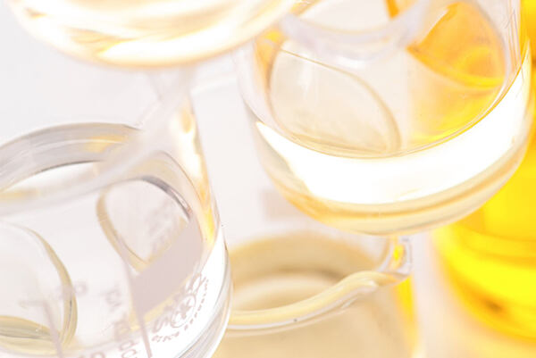 Sklenené laboratórne kadičky s makadamiovým olejom v zlatistých tónoch.