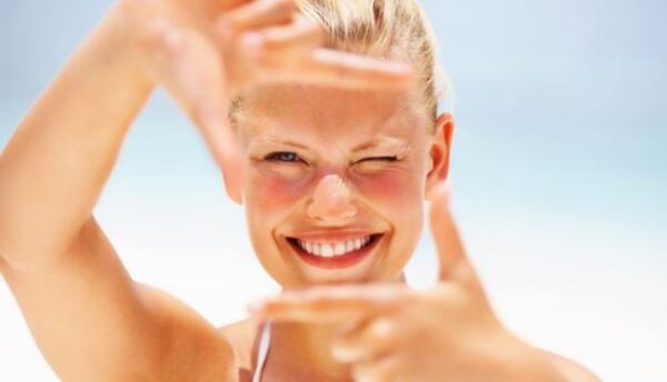 Usmiata žena na slnku si rukami vytvára rám pred tvárou a žmurká do svetla