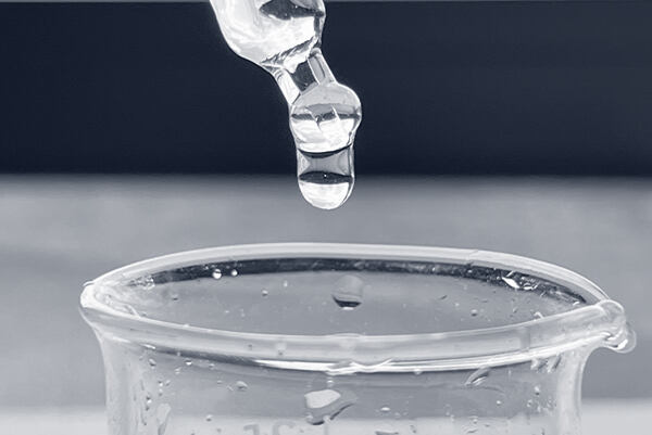 Kvapka číreho séra stekajúca z kvapkadla do laboratórneho pohára.