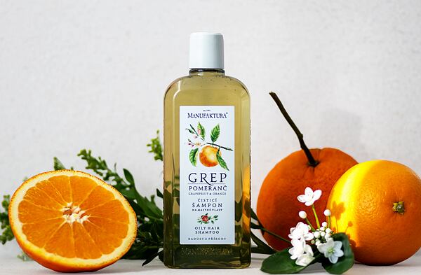 Čistiaci šampón Grep & Pomaranč od Manufaktury obklopený čerstvými pomarančmi a kvetmi na svetlom pozadí