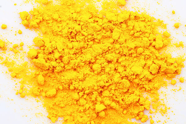 Jasne žltý prášok koenzýmu Q10 na bielom podklade.